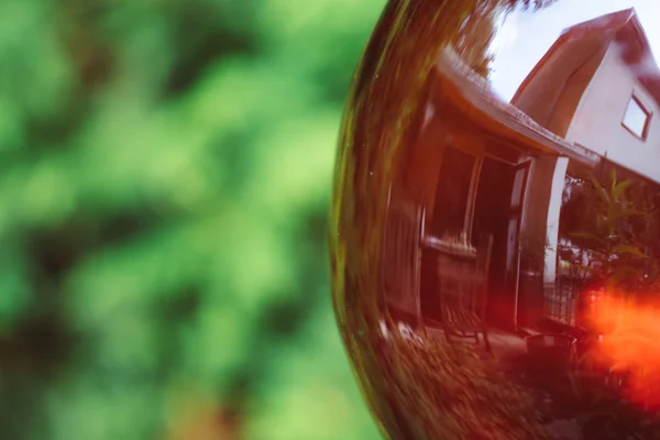 Reflection of house in red garden glass ball with green background