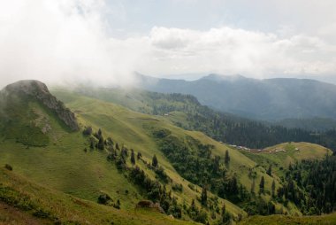 Küçük evler ve yollar çok altında aşağıdaki hillside bulutların üzerinde yeşil yoğun orman yalnız kulübe kapsayan dağlarındaki vadinin görünümü.
