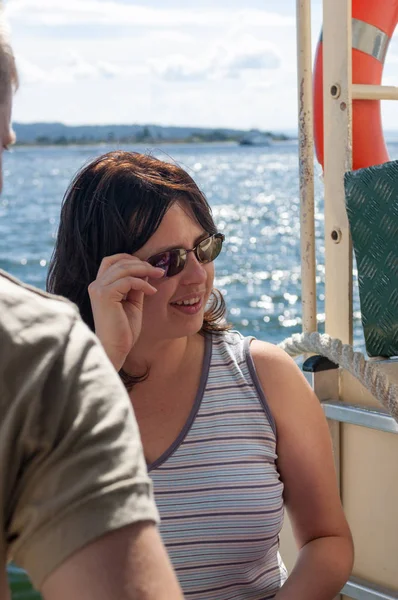 Güneş gözlüklü küçük bir feribot bir arkadaşıyla kırmızı lifebuoy ve mavi su sunscreens ile arka plan üzerinde siyah saçlı bir kızla.