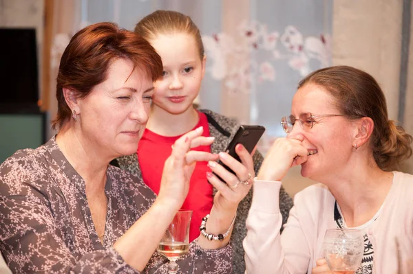 İki farklı yaşta kadınların ve küçük bir kız bir şey arıyoruz eğlenceli bir smartphone vasıl ev içinde
