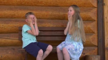 Çocuklar pat bir pasta oynarken, evde bir günlük duvar yakınında bir bankta otururken erkek ve kız kardeşi ve sarışın kız kardeşi