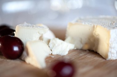 Keçi sütünden camembert tatlı kiraz çilek ile ahşap bir tahta üzerinde hala hayat dilimleri halinde kesilmiş. Planın üzerinde yatan net bir cam ile odak dışında