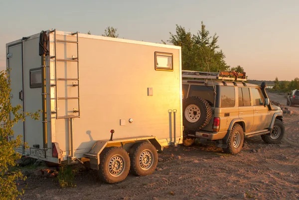 Remolque casero de dos ejes para caravanas todoterreno enganchado a un todoterreno en un camino de tierra en los rayos del sol poniente —  Fotos de Stock