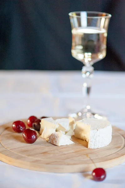 Keçi sütünden camembert tatlı kiraz çilek ile ahşap bir tahta üzerinde hala hayat dilimleri halinde kesilmiş. Arka planda bir kadeh beyaz şarapla
