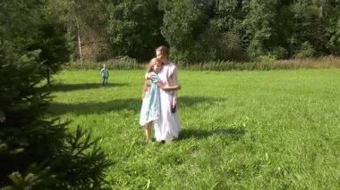 Annem elinde bir tasma ile çimenlikte duruyor. Çocuklar ona doğru koşar ve sarılır. Annem elinde bir tasma ile çim üzerinde duruyor çocuklar ona kadar koşmak, sarılmak ve gülerek bir şey tartışmak