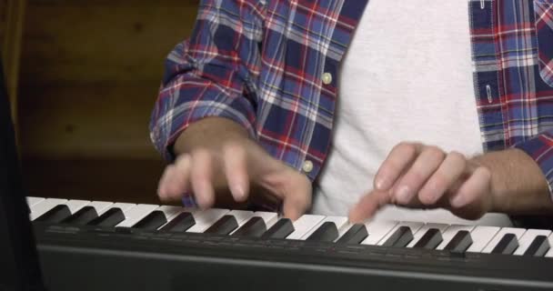 男性手在电钢琴键盘上弹奏节奏旋律的特写 前排为白色和黑色钢琴键 动作流畅 背景为白色T恤和蓝色 白色格子衬衫的双手细节 — 图库视频影像