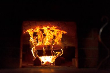 Bir Rus ocağının şömine kutusunda bir ateş alevleniyor. Rus ocağının fırınında canlı ateş, sağda metal bir kapı var, ön planda bir soba var..