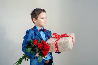 Buket kırmızı gül ve hafif bir arka plan üzerinde bir hediye ile sevimli gülümseyen çocuk.