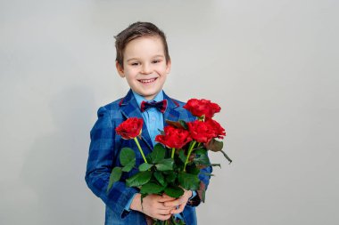 Sevimli küçük çocuk takım elbise ile hafif bir arka plan, St Sevgililer günü kavramı üzerinde elinde kırmızı gül buketi
