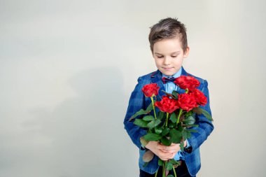 Sevimli küçük çocuk takım elbise ile hafif bir arka plan, St Sevgililer günü kavramı üzerinde elinde kırmızı gül buketi