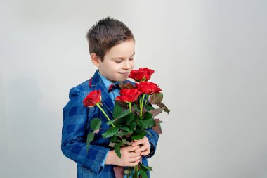 Sevimli küçük çocuk takım elbise ile hafif bir arka plan, St Sevgililer günü kavramı üzerinde elinde kırmızı gül buketi