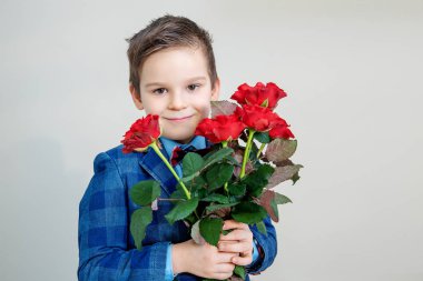Sevimli küçük çocuk takım elbise ile hafif bir arka plan, St Sevgililer günü kavramı üzerinde elinde kırmızı gül buketi