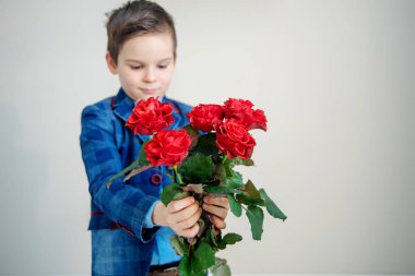 Sevimli küçük çocuk takım elbise ile hafif bir arka plan, St Sevgililer günü kavramı üzerinde elinde kırmızı gül buketi
