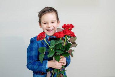 Sevimli küçük çocuk takım elbise ile hafif bir arka plan, St Sevgililer günü kavramı üzerinde elinde kırmızı gül buketi