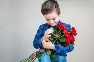 Adorable little boy in suit with a bouquet of red roses in hands on a light background, st. valentine's day concept