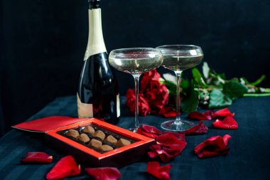 two glasses of wine, rose, petals and chocolates on a black background. St. Valentine's Day, 8 March and Mother's Day concept