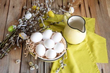 Ahşap masa üzerinde sarı plaka beyaz yumurta ile söğüt dallarında Paskalya yortusu yumurta