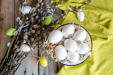 Ahşap masa üzerinde sarı plaka beyaz yumurta ile söğüt dallarında Paskalya yortusu yumurta