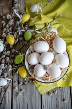 Ahşap masa üzerinde sarı plaka beyaz yumurta ile söğüt dallarında Paskalya yortusu yumurta