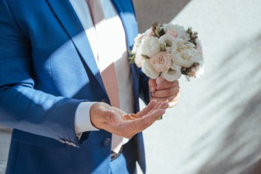 Damat eli buketi tutuyor taze çiçekler pembe ve beyaz renklerle kaplanıyor ve elinde iki altın yüzük var.