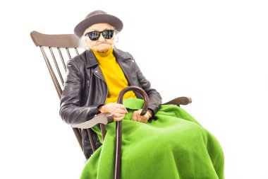 Old woman with hat and sunglasses sitting on the chair coverd with green blacket. clipart