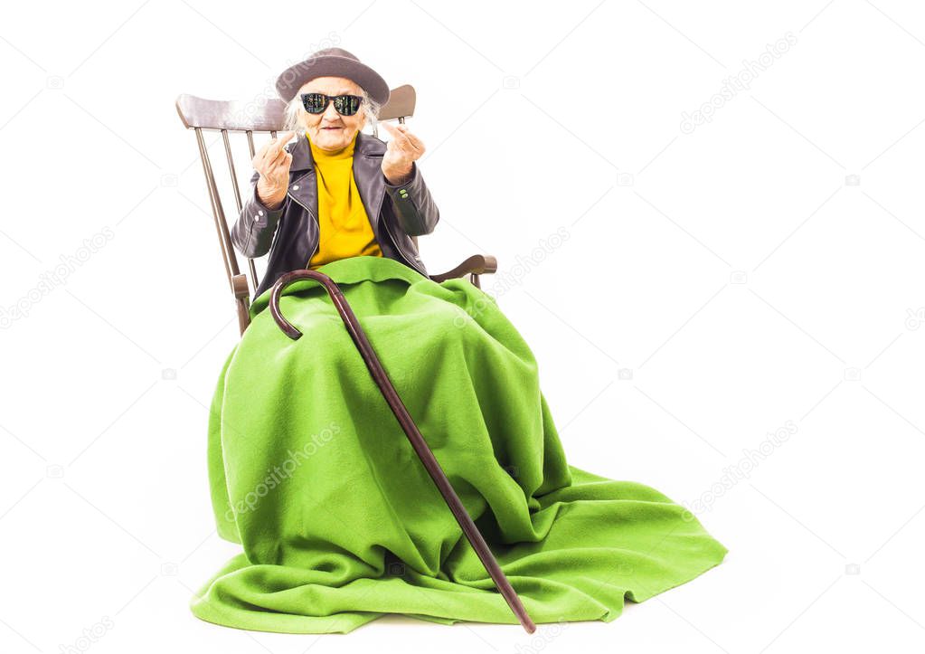 Old woman with hat and sunglasses sitting on the chair coverd with green blacket.