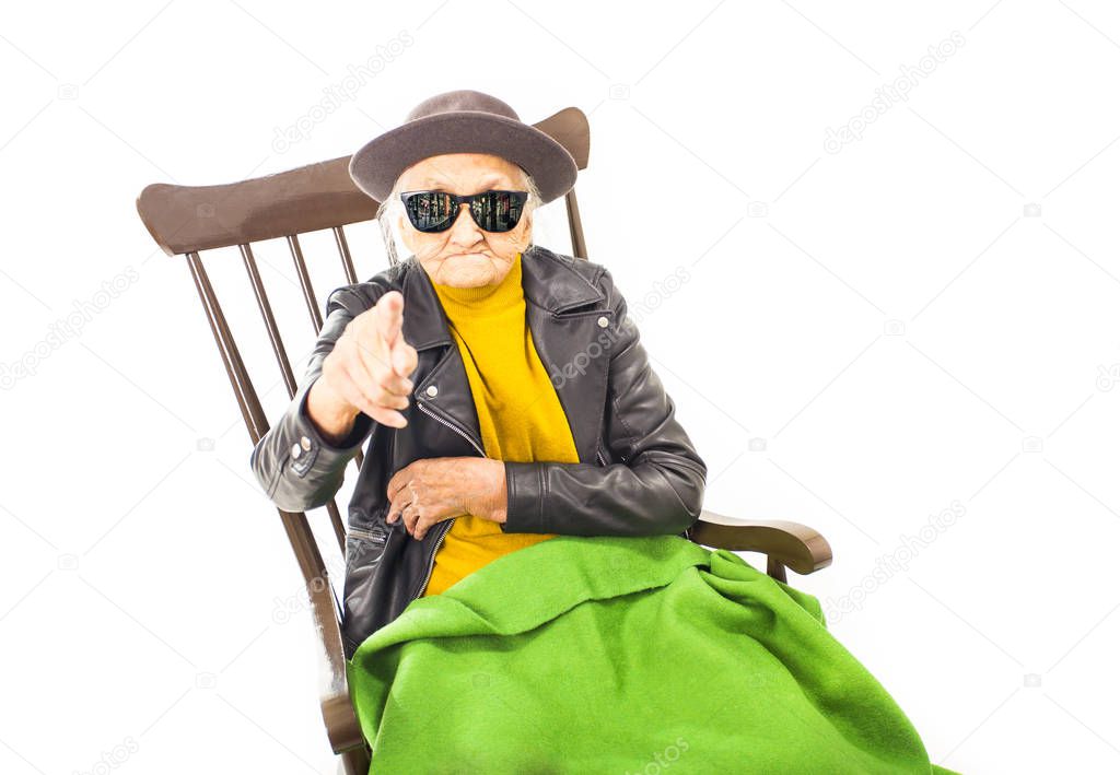 Old woman with hat and sunglasses sitting on the chair coverd with green blacket.