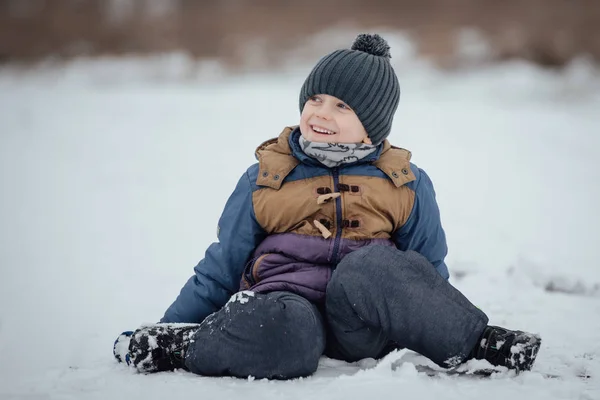 Έξι Χρονών Αγόρι Χαμογελά Και Κάθεται Στο Χιόνι — Φωτογραφία Αρχείου