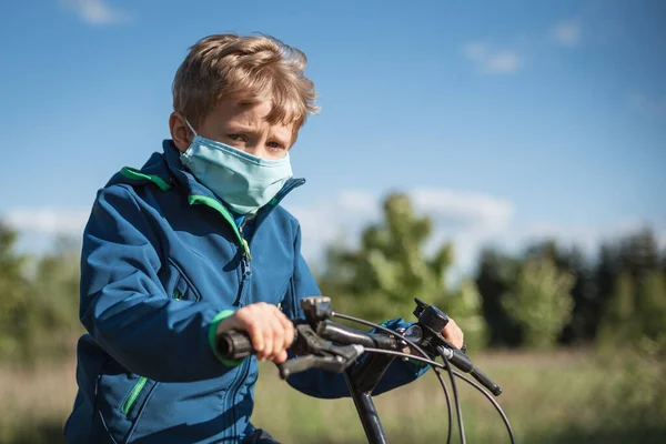 Young boy riding on bicycle with face mask due to pandemic Covid-19.