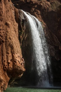 Faslı genç bir adam şelalenin altındaki suya atlamadan önce kayaya tırmanır..