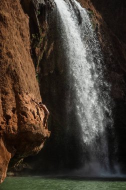 Faslı genç bir adam şelalenin altındaki suya atlamadan önce kayaya tırmanır..