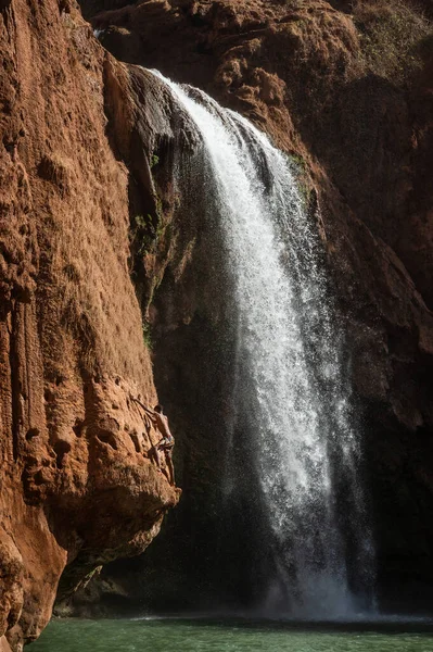 Faslı genç bir adam şelalenin altındaki suya atlamadan önce kayaya tırmanır..