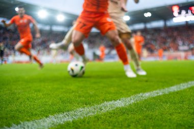 Stadyumdaki futbol sahasında çimen ve kenar çizgisinde ve arka planda oyuncunun bacakları.