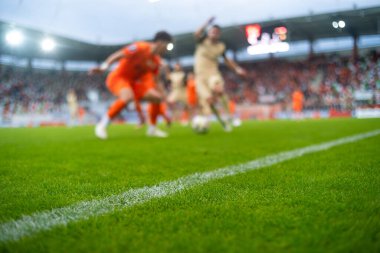 Stadyumdaki futbol sahasında çimen ve kenar çizgisinde ve arka planda oyuncunun bacakları.