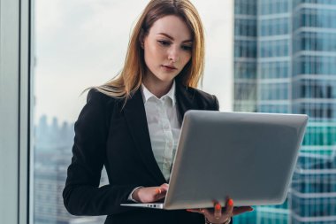 İş bölgesi manzaralı panoramik pencere karşı bir laptop ayakta tutan lüks ofisinde çalışan genç kadın avukat