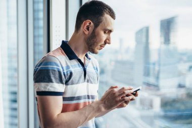 Office penceresinde tarafından Smartphone ayakta tutan işadamı