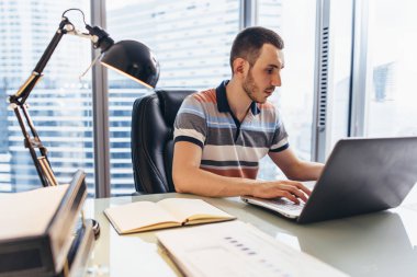 Ofiste masada oturan bilgi için internet arama kullanarak dizüstü bilgisayar üzerinde çalışan iş adamı