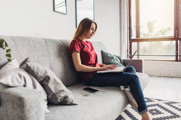 Hermosa joven sentada en el sofá y el uso de la computadora portátil en casa — Foto de Stock