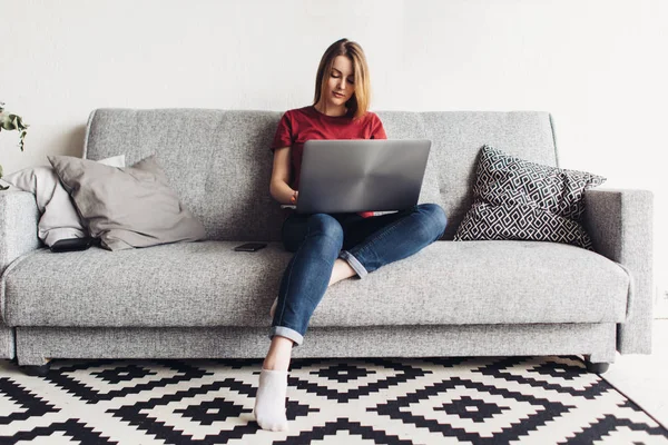 Kvinna som använder bärbar dator sitter på soffan i vardagsrummet — Stockfoto