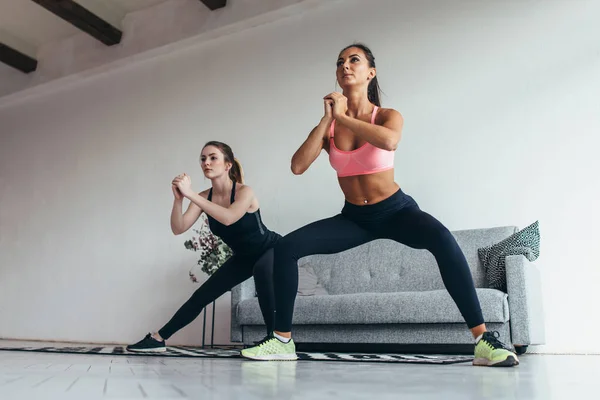 Två passar flickor gör träning utför laterala utfall hemma. — Stockfoto