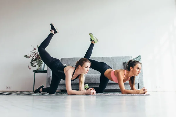 Två passa kvinnor gör böjt knä åsna sparka motion i alla fyra position tränar sina skinkor hemma — Stockfoto