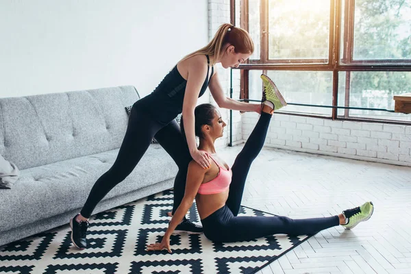 Mujer en forma haciendo ejercicios de estiramiento con la ayuda de un amigo sosteniendo su pierna en casa — Foto de Stock