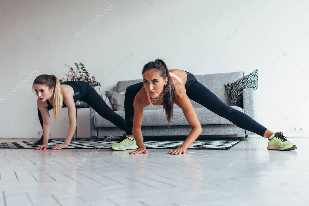 Two fit girls doing home workout performing lateral lunges at home.