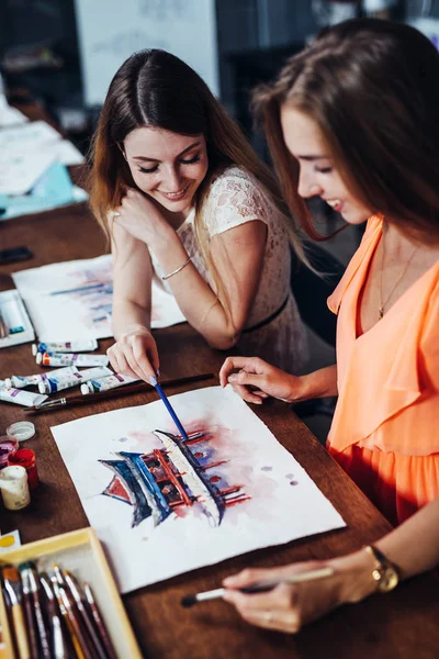 Две молодые женщины, посещающие уроки акварельной живописи для взрослых в художественной школе. Девушка, показывающая свои работы другу . — стоковое фото