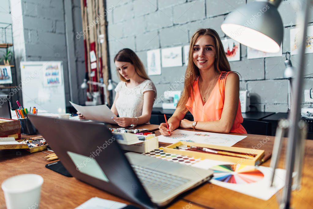 Designers workspace. Two female artists drawing decorative elements sitting at desk in creative studio.