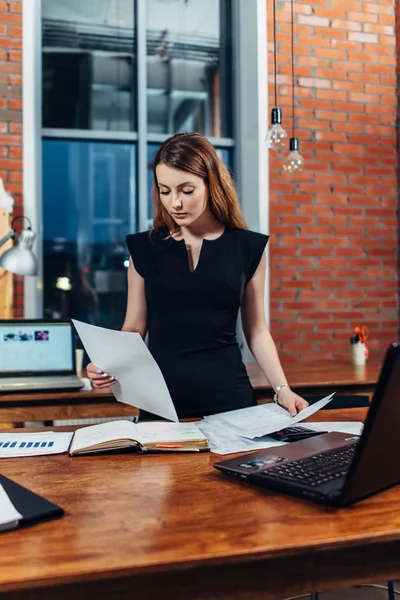 Femme sérieuse lecture de documents d'étude reprend debout au bureau dans un bureau élégant — Photo