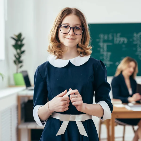 Porträtt av leende skolflicka med krita i hennes händer som står i klassrummet — Stockfoto