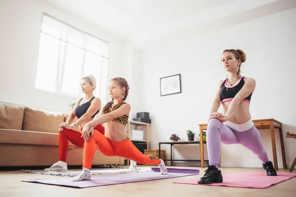 Женщины сидят на корточках и разминают ноги, выполняя упражнения на мышцах задницы. — стоковое фото