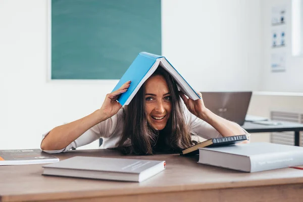 Estudante alegre esconde sua cabeça sob o livro sob o livro — Fotografia de Stock