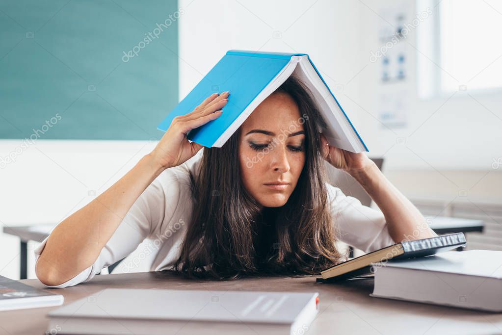 Tired girl studying at working table. Exhausted female student reading books.